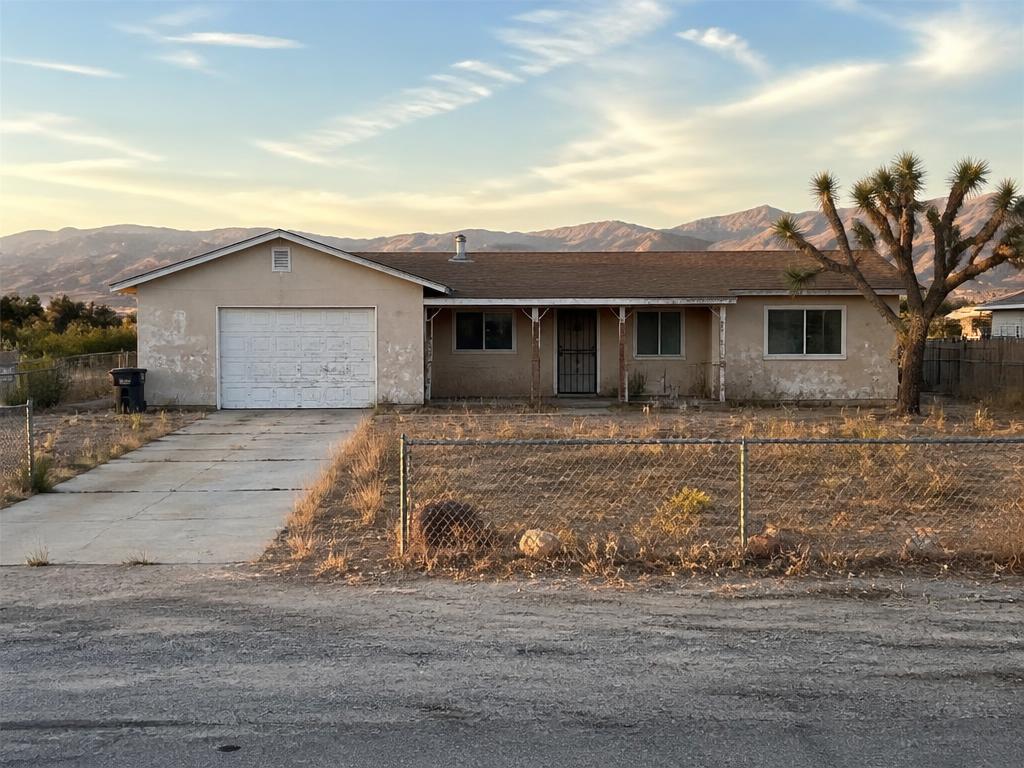 Distressed single-story Antelope Valley ranch home with faded stucco, desert yard, and mountains at golden hour