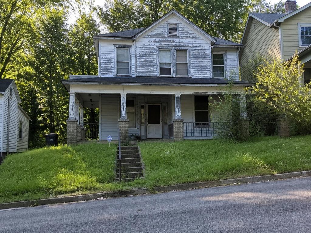Distressed two-story Birmingham home with weathered siding, sagging porch, and overgrown yard